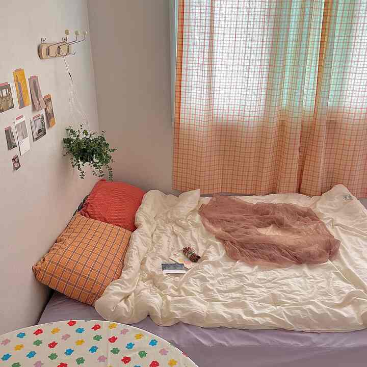 暖かいオレンジとアイボリーのトーンの小さな寝室、整ったベッドとチェック柄のカーテンが調和した居心地の良い空間