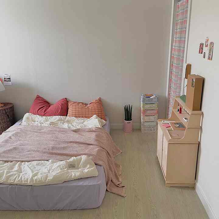 ベージュとライトブラウンのトーンの寝室、中央にベッドと枕が配置され、隣にキャビネットがある雰囲気のあるインテリア