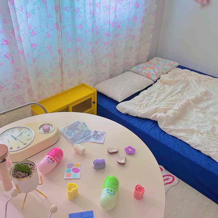 白と青を基調とした寝室、ベッドと花柄カーテン、テーブル上の多彩な小物が配置されたシンプルで落ち着いたインテリア