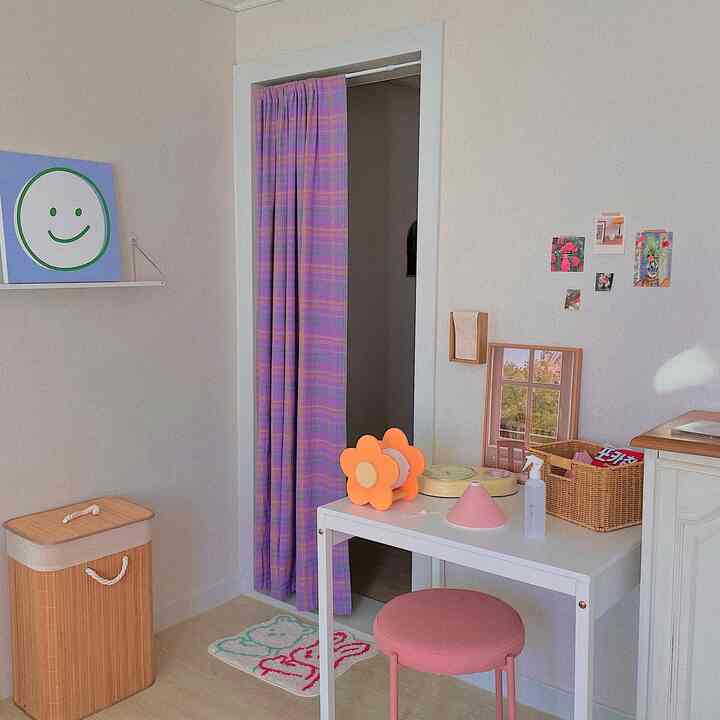 白とピンクの色調の小さな部屋、カーテンとデスク、スツールが配置された印象的な一人暮らしの空間
