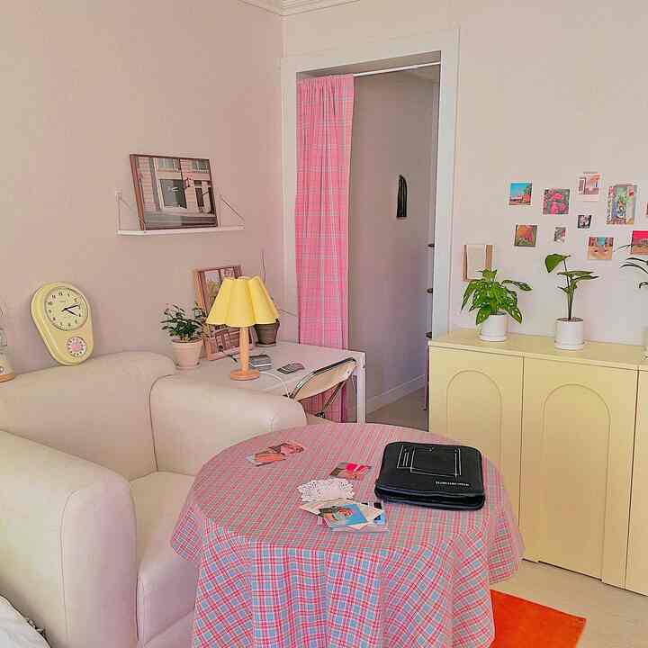 ピンクチェックのカーテンとテーブルクロス、黄色のキャビネットとランプが配置された雰囲気のあるリビング