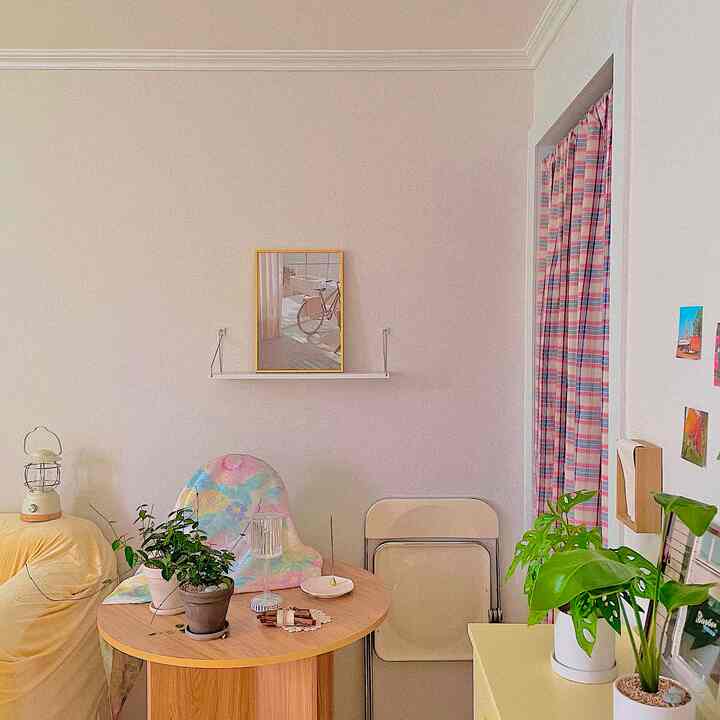 ベージュとイエローの色調が特徴のワンルームダイニングルーム、木製のダイニングテーブルとカラフルなカーテン、植物が配置された温かみのある空間