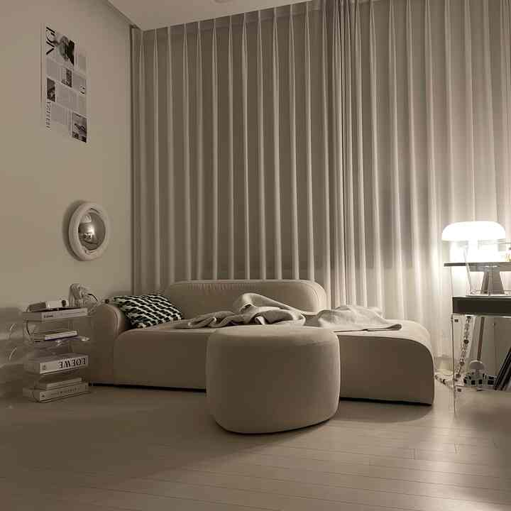 柔らかなベージュと白の色調のリビング、モダンなラウンジソファとアクリルのサイドテーブル、暖かな照明のあるシンプルな空間