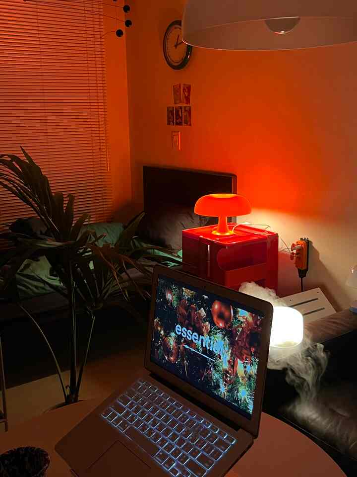 暖かいオレンジ色のムード照明が灯るワンルームのリビング、ベッドとソファ、マックブック、ムード加湿器が配置された雰囲気のあるインテリア