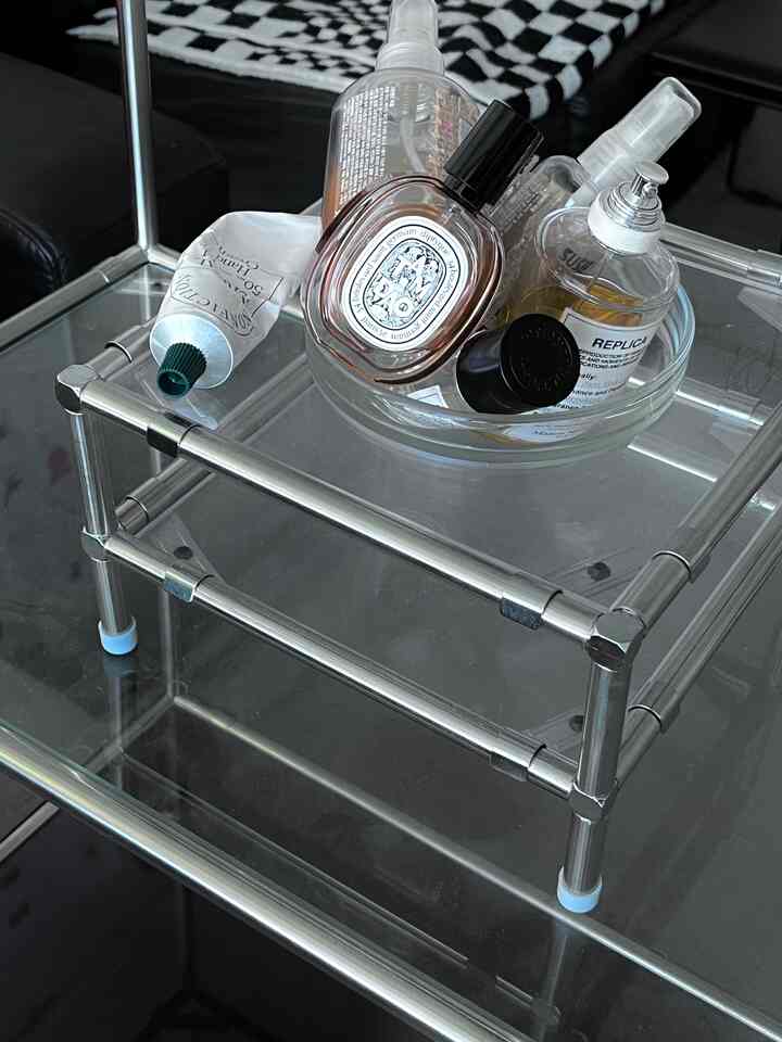 シルバーパイプ構造と透明なガラス棚に香水とクリームが置かれたモジュール家具があるモダンでミニマルな空間