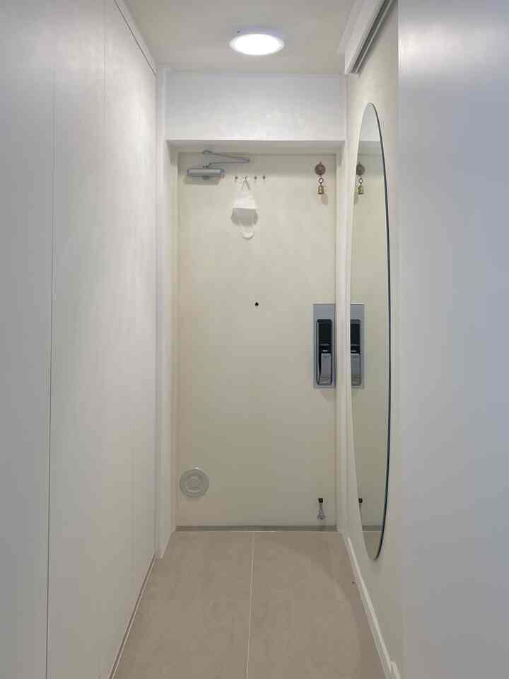 白を基調とした狭い玄関、シンプルな靴収納と大きな楕円形の鏡が配置された清潔感のあるインテリア