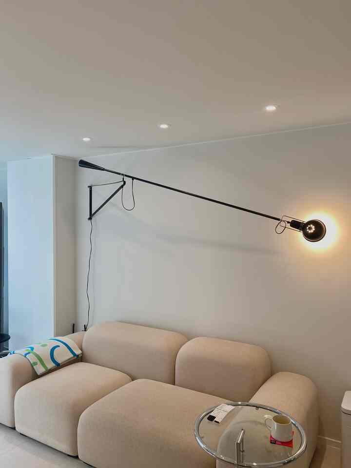 白い壁とベージュのソファ、黒いブラケットライトが配置されたモダンなリビング空間