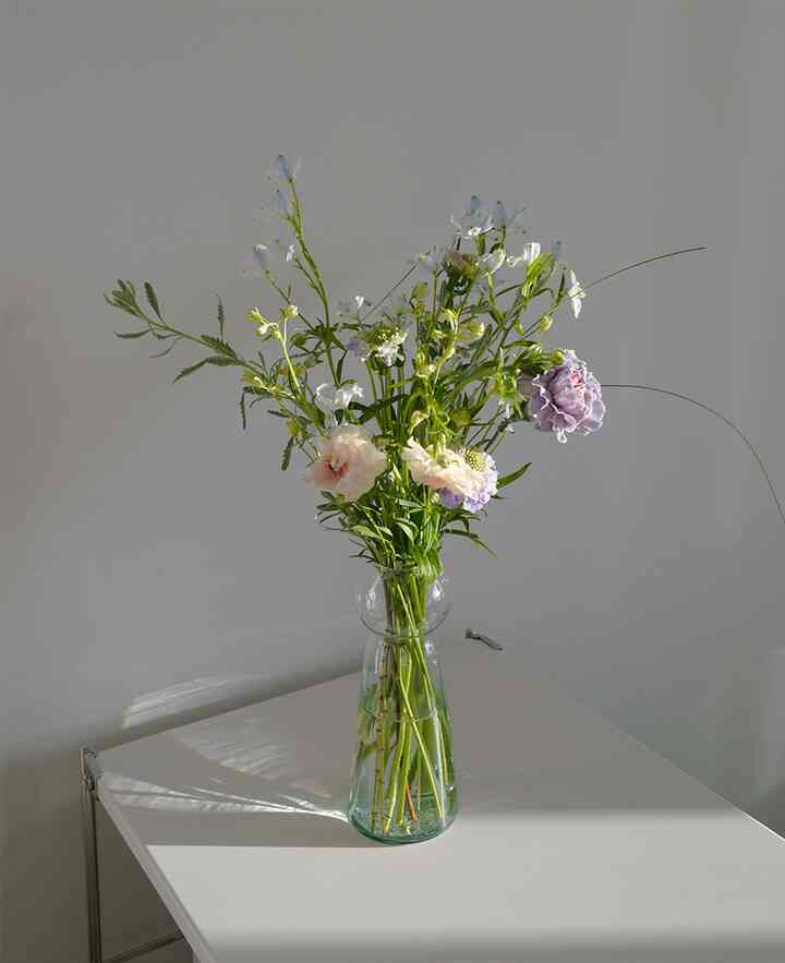 白い背景とテーブルの上に透明な花瓶と様々な生花が置かれたシンプルな寝室の空間