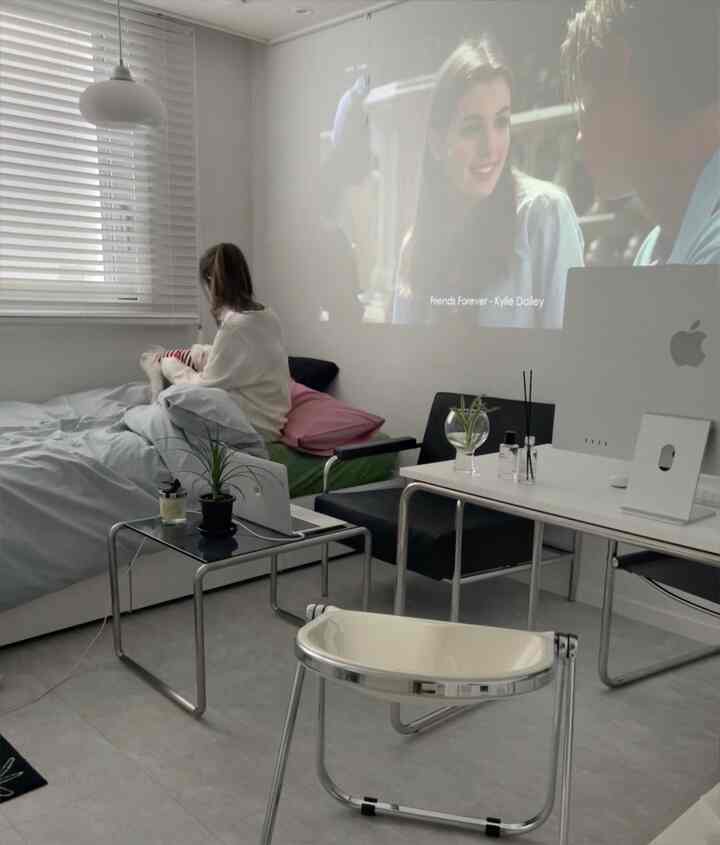 ホワイトとグレーのトーンの寝室兼ホームオフィス、ベッドにペットと人物がいて、ミニマルでモダンな雰囲気のあるインテリア