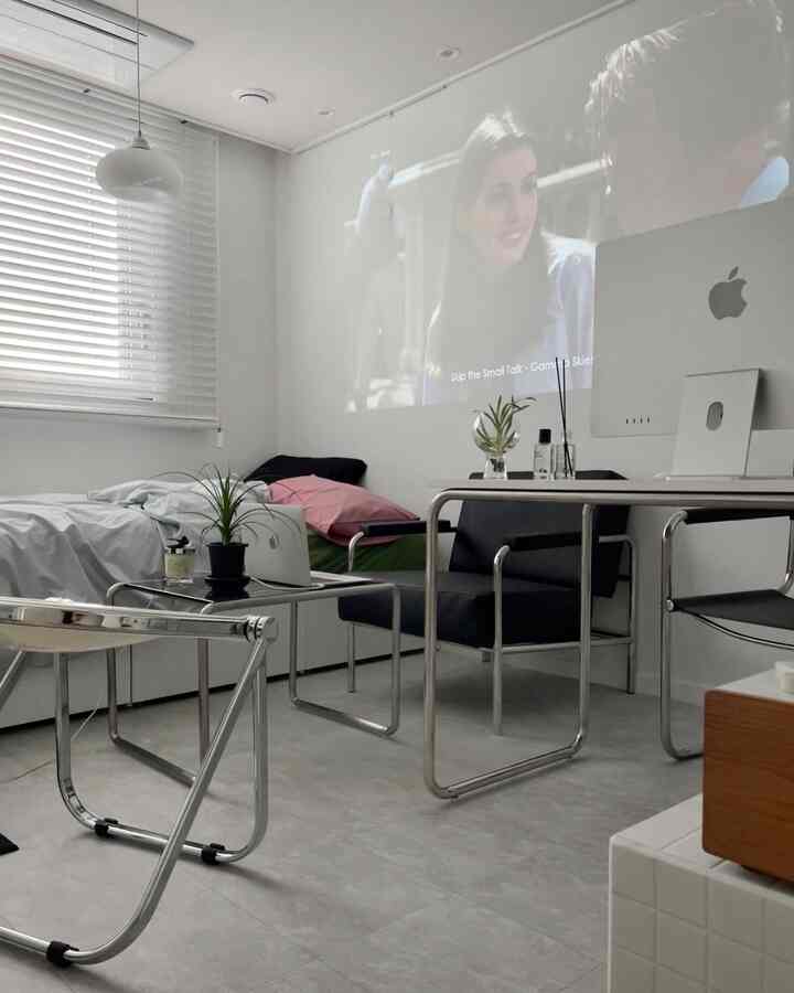 白とグレーのトーンの一人暮らし向け寝室兼ホームオフィス、ミニマルな机とベッドが配置されたすっきりとした空間