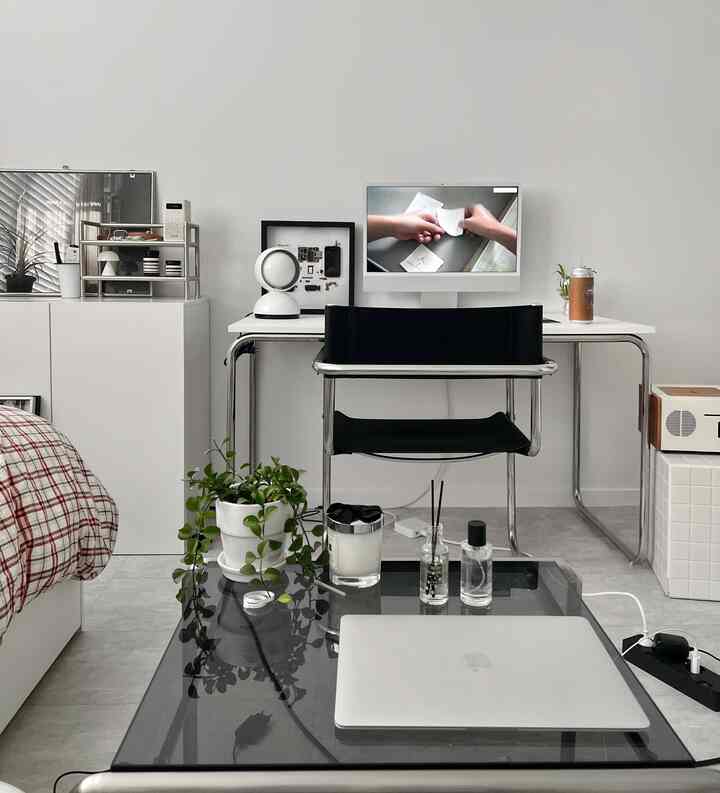 ホワイトトーンのホームオフィス、白いデスクとオフィスチェア、ノートパソコンと植物が配置されたミニマルな空間