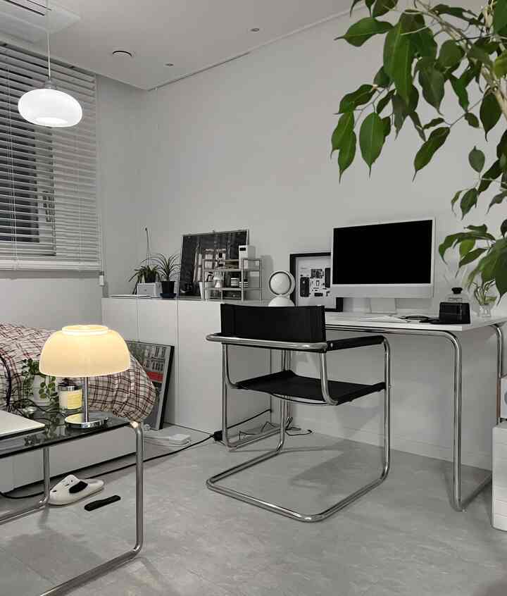 ホワイトとライトグレーのトーンのワンルームホームオフィス、ブラックのオフィスチェアとテーブルランプが配置されたシンプルでモダンなインテリア