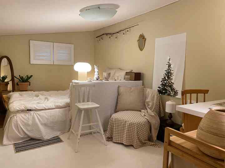 ベージュと白を基調とした小さな寝室、ベッドとアームチェア、テーブルランプが配置された温かみのあるナチュラルなインテリア