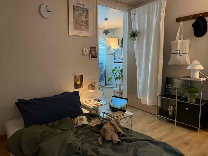 ホワイトとブラウンのトーンの寝室、ベッドとノートパソコン、空間を区切る白いカーテンが配置された落ち着いた雰囲気のインテリア