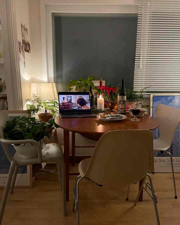 木目調とホワイトの色調のダイニングルーム、丸いダイニングテーブルと椅子、キャンドルと植物が配置された居心地の良い空間