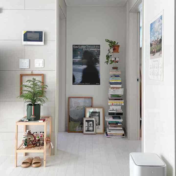 白と木目調のリビング入り口、積み重ねられた本棚と額縁が配置されたシンプルで自然な雰囲気のインテリア