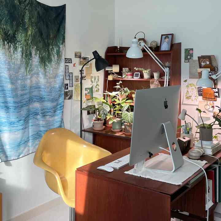 ライトグレーの壁と床のホームオフィス、ヴィンテージ風の木製デスクと黄色の椅子、植物が配置された雰囲気のあるインテリア