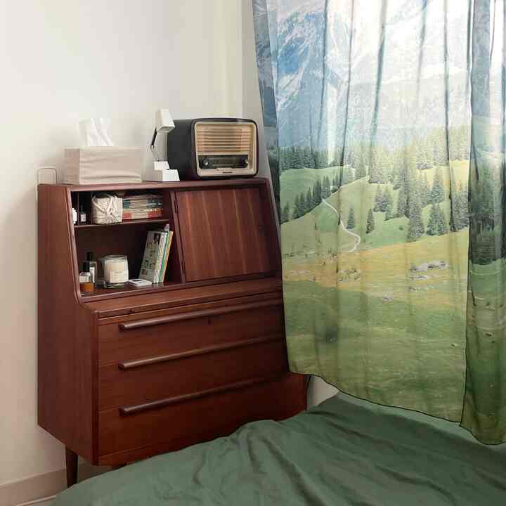 ブラウンの木製ドレッサーと自然の風景カーテンがある雰囲気のある寝室