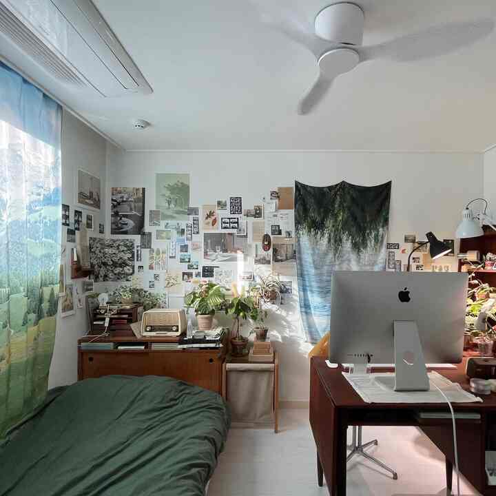 ホワイトの壁と木目調家具が並ぶ一人暮らし向けの寝室兼ホームオフィス、植物とウォールデコが調和した落ち着いた空間