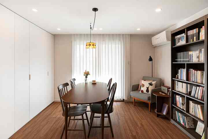 ホワイトとブラウンの色調のリビング、壁面収納とダークウッドのダイニングテーブル、本棚、アームチェアが配置された雰囲気のあるインテリア