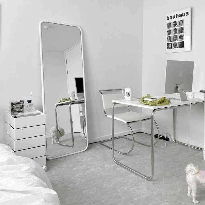 白を基調とした小さなホームオフィス、ミニマルな家具と大きな全身鏡が配置された清潔感のあるインテリア
