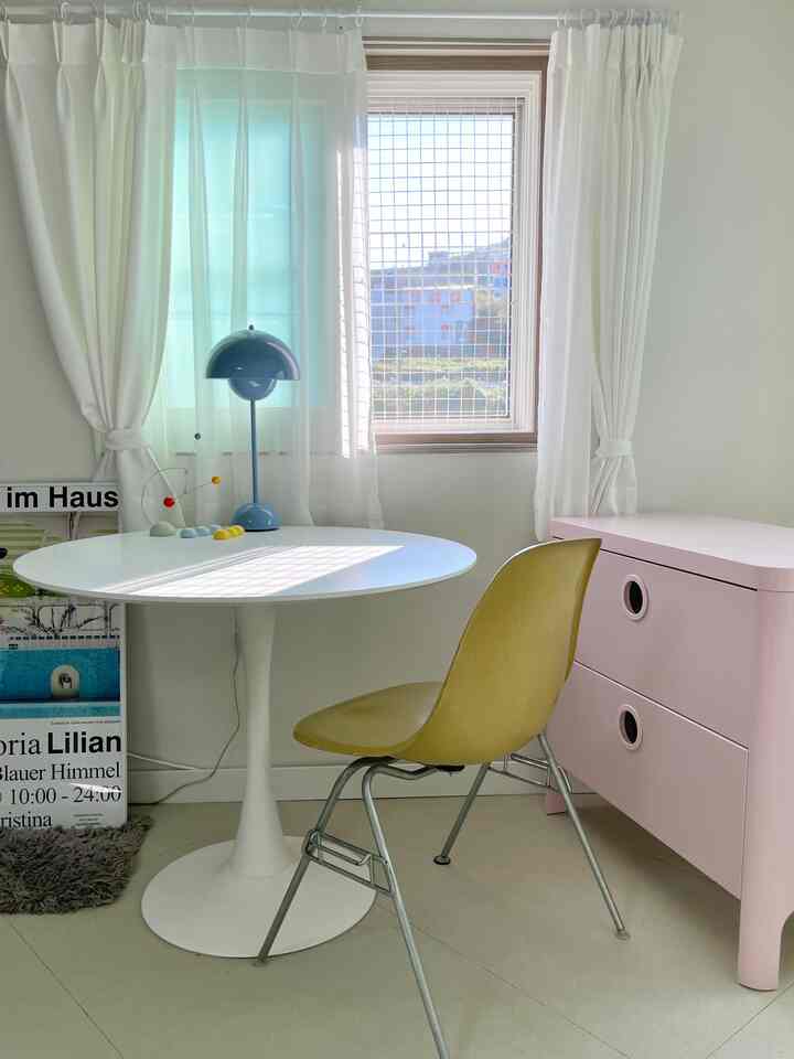 白とピンクのトーンのダイニングルーム、丸テーブルと子供用チェストが配置された明るく居心地の良い空間