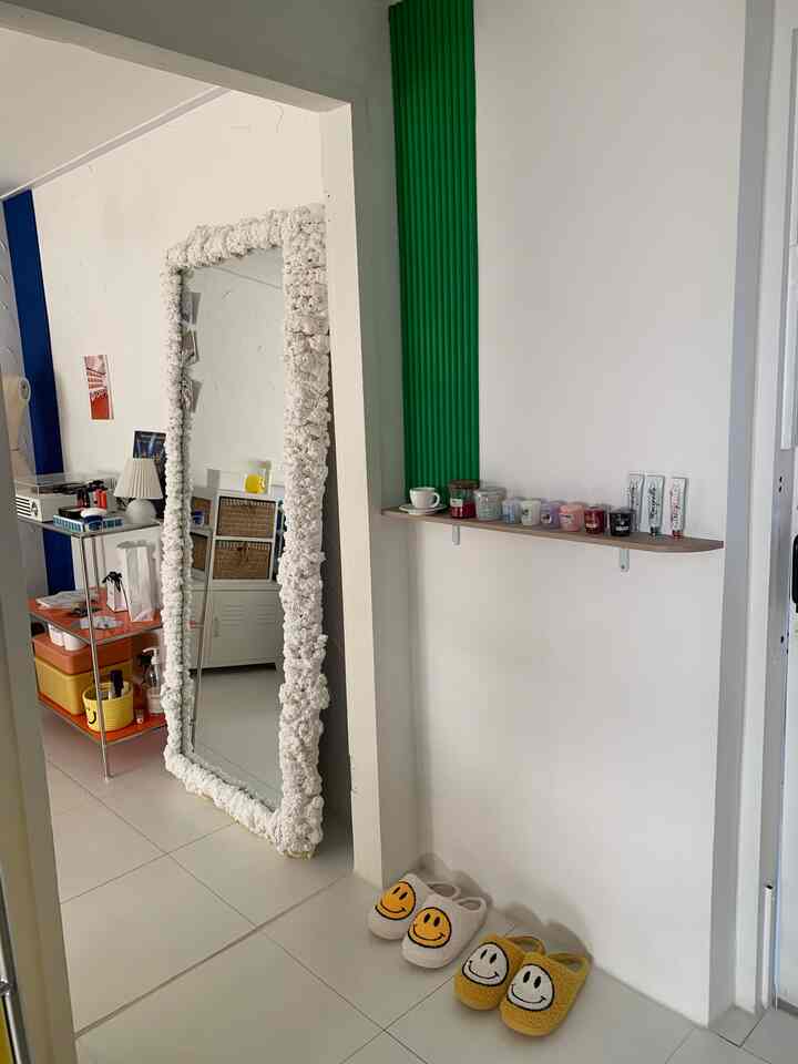 ホワイトを基調としたリビング、グリーンのアクセントウォールがあり、壁棚と額縁の鏡、スマイル柄のスリッパが整然と並ぶ雰囲気のある空間