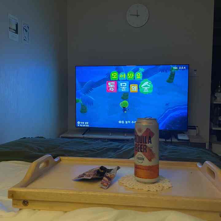 ベージュとナチュラルカラーの寝室、大型テレビと木製ベッドトレイが配置された落ち着いた雰囲気の空間