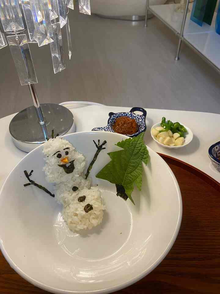 白と木目調の調和したキッチン、かわいい雪だるま型のご飯と調味料、葉が配置された印象的なワンルームの空間