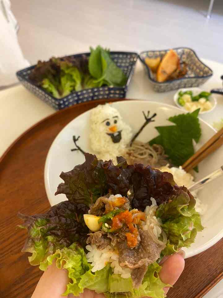 ウッド調の丸いトレイの上に葉野菜やご飯、肉、そしてオラフの形をしたご飯の飾りが置かれた、雰囲気のあるおうちカフェ風のダイニングシーン