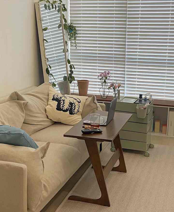 ベージュの色調のリビングルーム、ベージュのソファと木製のサイドテーブル、収納トロリーが配置された居心地の良い自然な雰囲気のインテリア