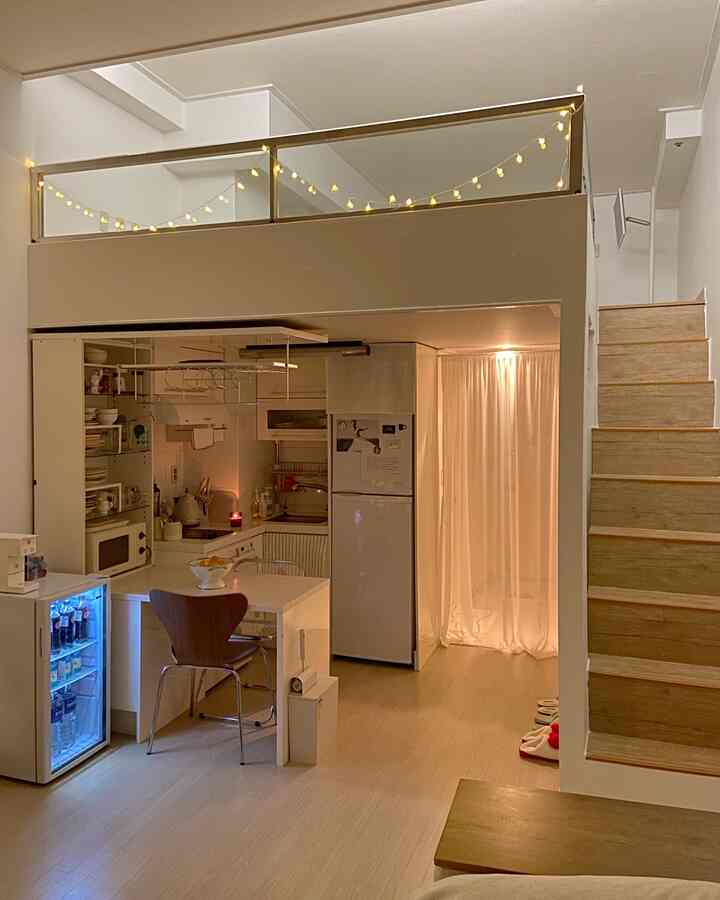 ホワイトとウッドトーンが調和したロフト付きワンルームキッチンスペース、リカー冷蔵庫とカーテンで覆われた収納が配置された居心地の良い雰囲気のインテリア