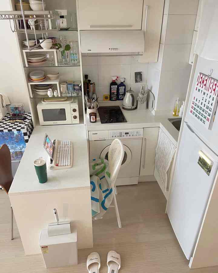 明るいホワイトのトーンが特徴的なコンパクトなキッチン、電子レンジやケトル、ダイニングチェアが整然と配置されたインテリア
