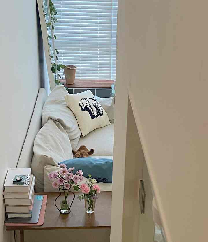 ベージュトーンのリビング、ベージュのソファと木製サイドテーブル、花瓶に生けた花が明るい雰囲気の室内