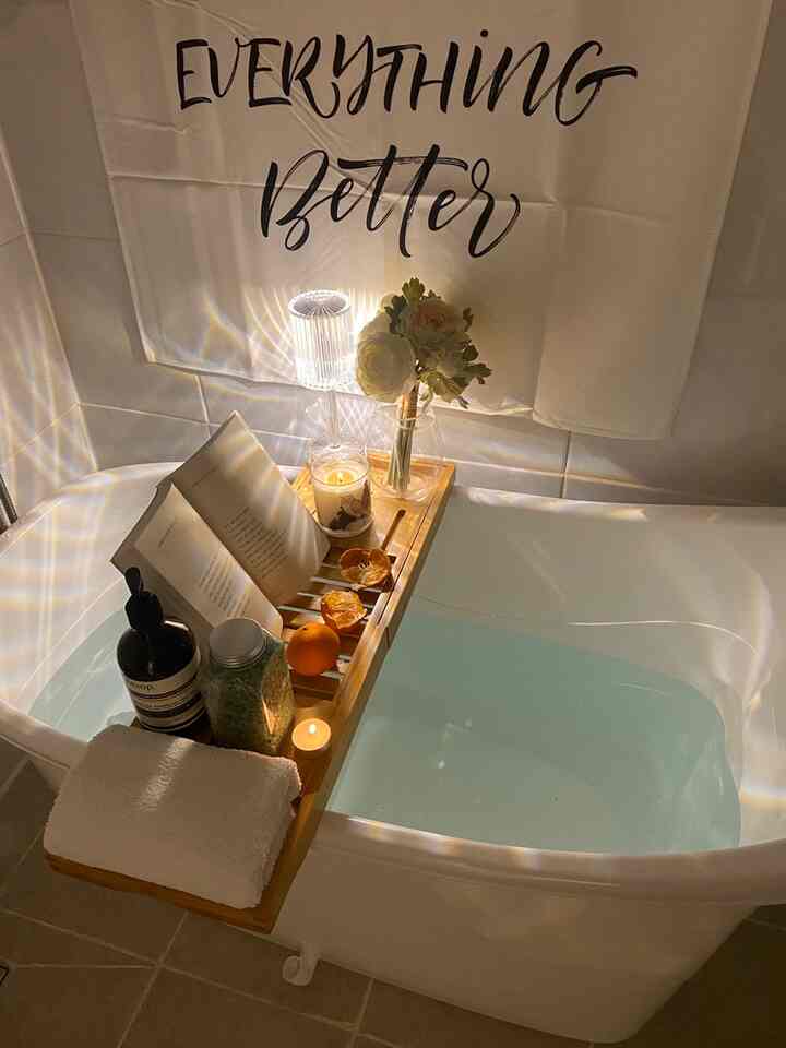 白いトーンの浴室、移動式バストレイに本やキャンドル、花瓶、タオルが置かれた雰囲気ある半身浴空間