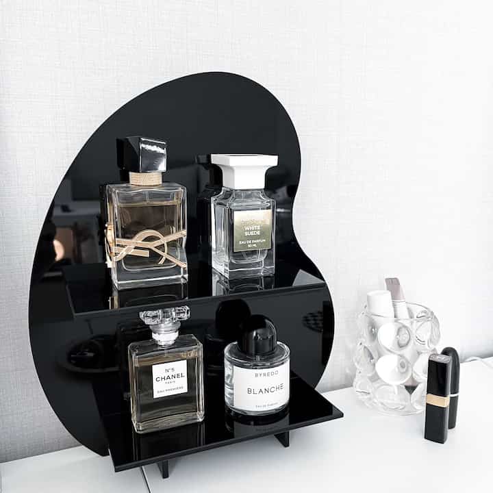 透明なブラシホルダーと黒い棚に置かれた高級香水がある清潔感のある化粧台の空間