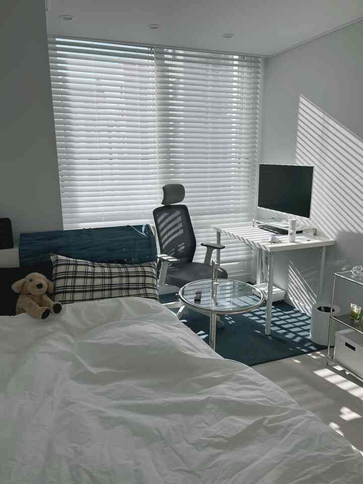 白を基調とした寝室、窓辺にオフィスチェアとデスクが配置された清潔感のある空間