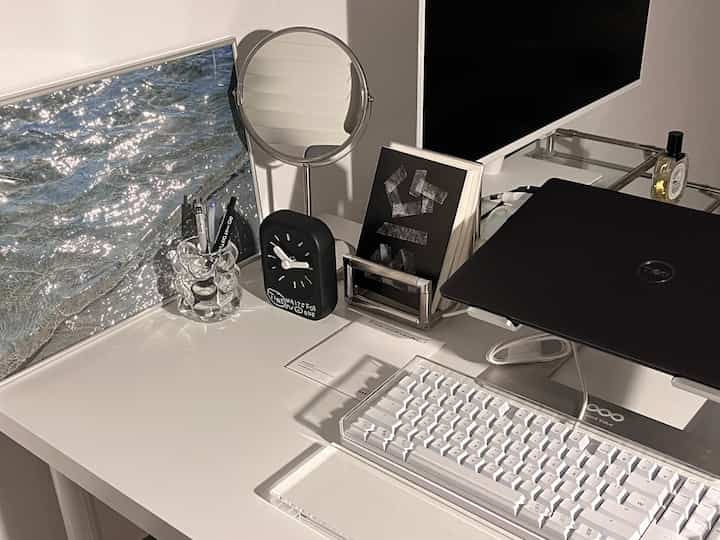 白と黒のトーンのホームオフィス、白いデスクにキーボードとモニター、鏡が配置され、清潔で機能的な作業環境を演出している