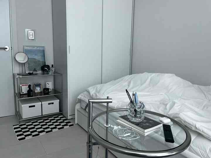 白と銀色のモダンな小さな寝室、スライド式のワードローブとガラス製のメタルサイドテーブルが整然と配置された空間