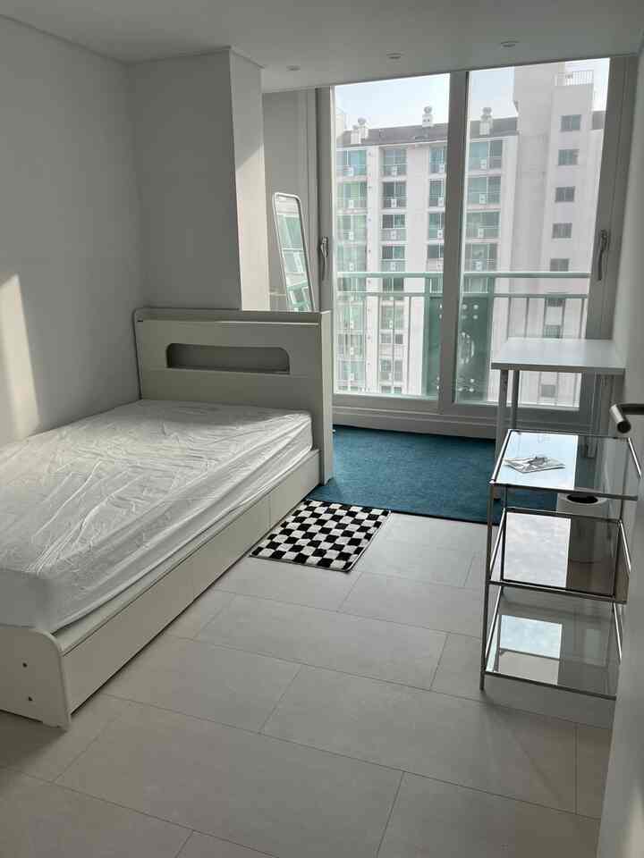 ホワイトとナチュラルトーンの一人用ワークスペース、ベッド、デスク、全身鏡、青いラグが配置された清潔な部屋