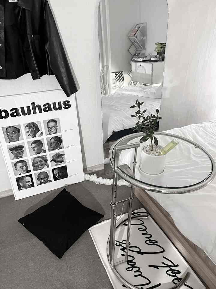 白と黒のトーンの寝室、大きな円形の鏡と円形ガラストップのサイドテーブルが配置されたミニマルでモダンな空間