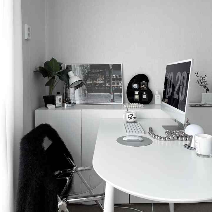 ホワイトトーンのモダンなホームオフィス、パソコンが置かれた清潔なデスク、スタイリッシュなキャビネット、植物と照明が配置された実用的な空間