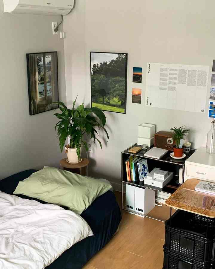 ナチュラルな木目調の床とネイビーの寝具があるワンルーム寝室、棚やポスターが配置された雰囲気のある空間