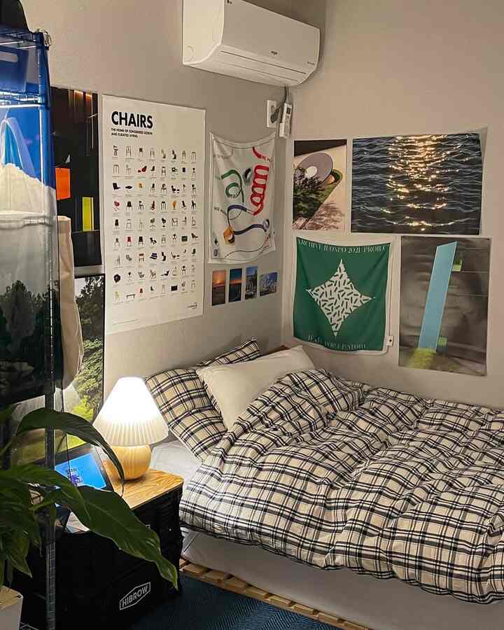 ネイビーとベージュのトーンのワンルーム寝室、チェック柄の寝具と多様なポスターが配置された印象的な空間