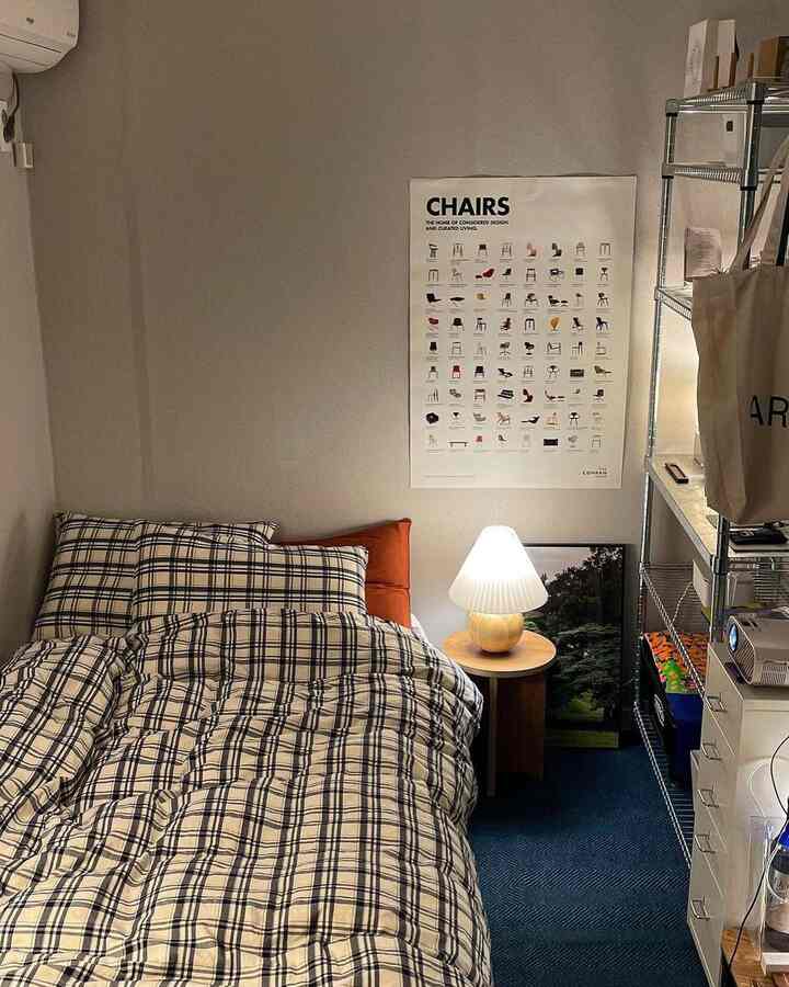 ネイビーのラグが敷かれた寝室、チェック柄の寝具と丸いナイトテーブルに置かれたランプが印象的なモダンで温かみのある空間