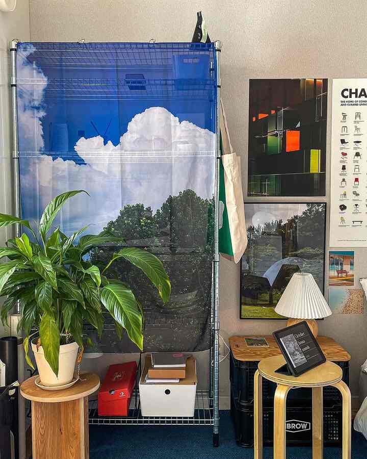 青いファブリックポスターで覆われたイケアの金属棚と観葉植物、スツールが配置された落ち着いた室内空間