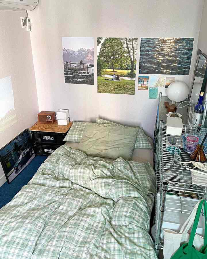 アイボリー色の壁とベッドリネンが配置されたコンパクトな寝室。壁に複数のポスター、金属製シェルフ上のオブジェが調和している空間