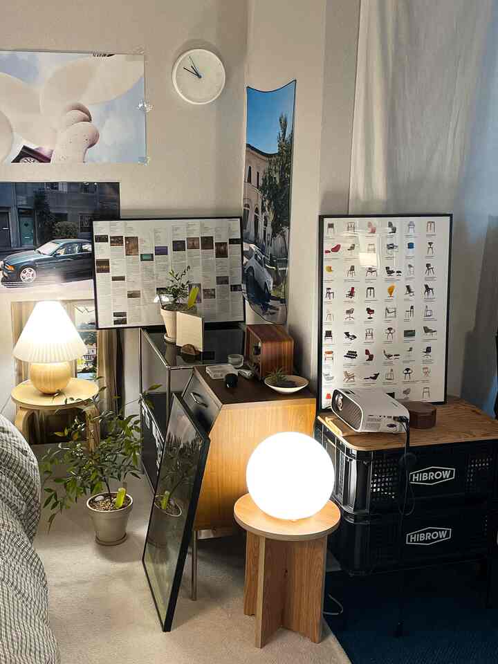 白い壁とブラウンの木製家具が主役の狭い部屋、ナイトテーブルとスツールに置かれた丸い照明が暖かいレトロな雰囲気を演出