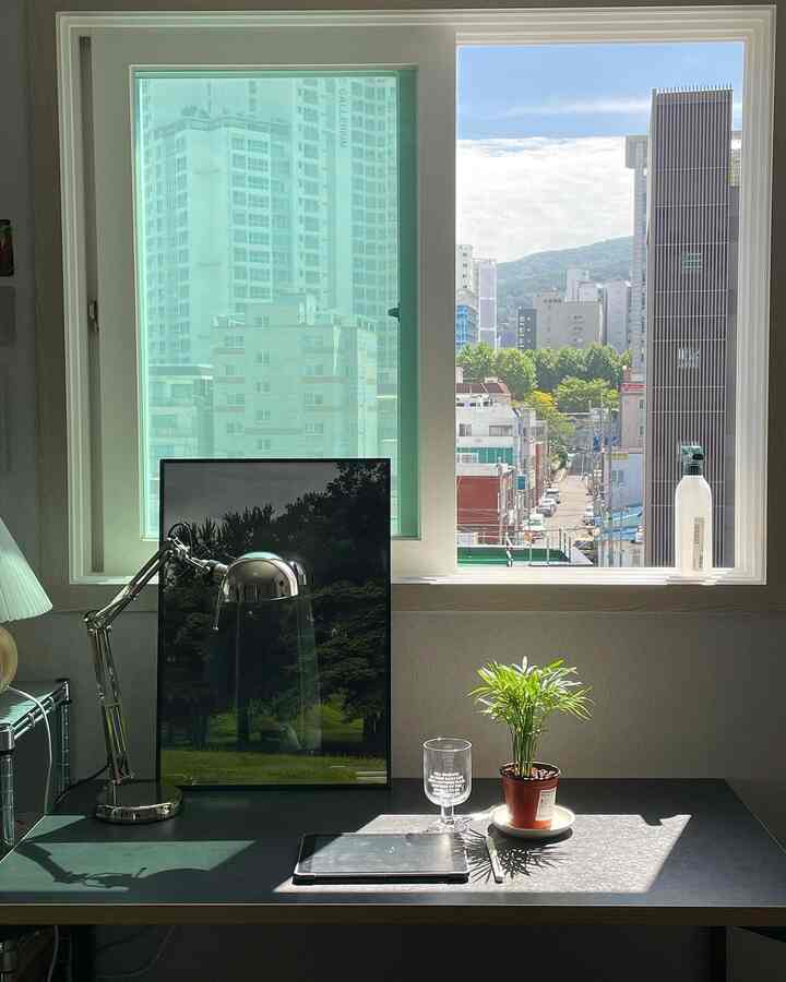 自然光が差し込む白い壁のホームオフィスデスク、黒いデスクの上にテーブルランプ、植物、タブレットが置かれた清潔感のある作業空間