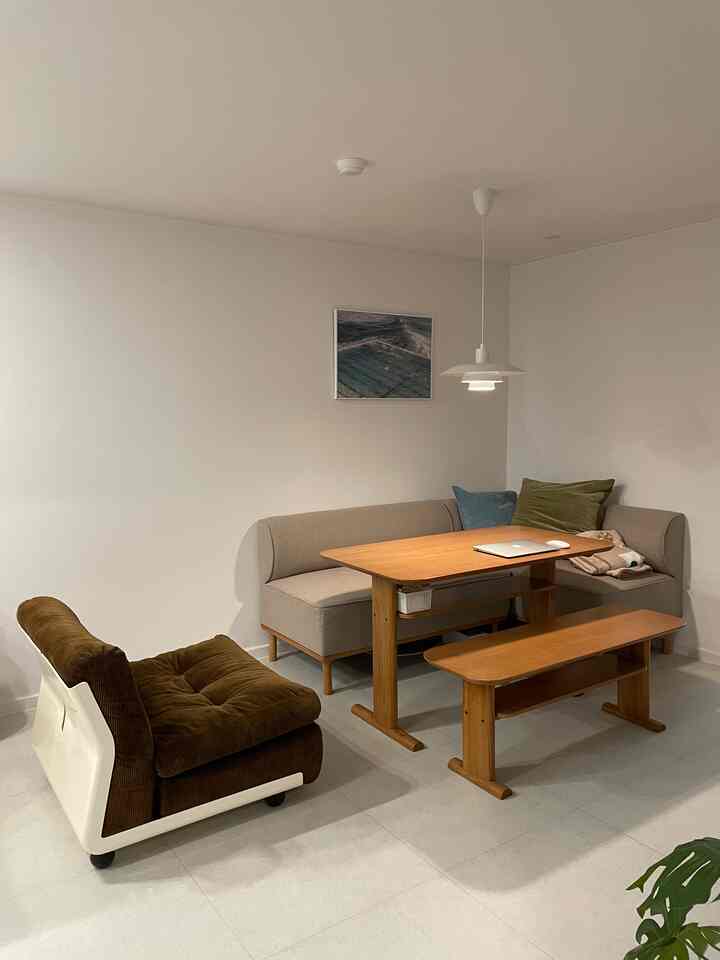 白い壁とライトグレーの床のリビング、ベージュのソファと木製のダイニングテーブルセットが配置されたナチュラルモダンな印象の空間